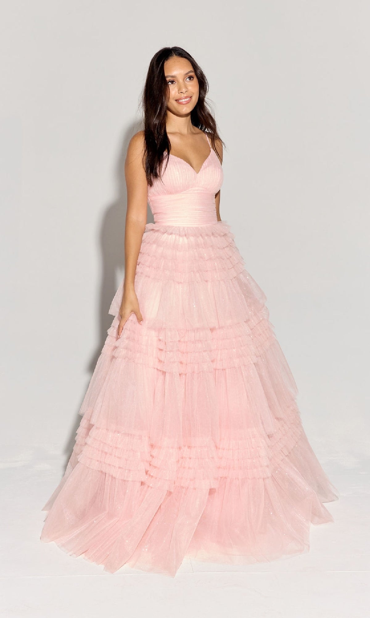 A woman stands against a plain background wearing the Lace-Up Long Glitter-Tulle Prom Dress: Eureka 9888, featuring tiered layers, a fitted bodice, and a sleeveless, floor-length glitter tulle design.